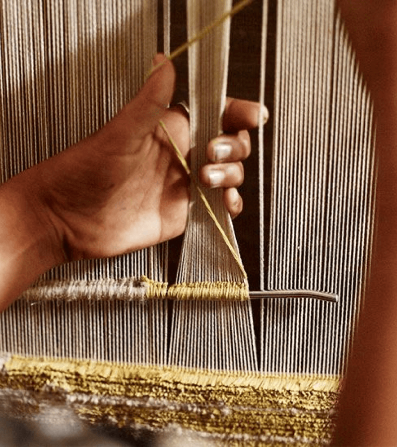 Close-up of hands working with golden threads on loom