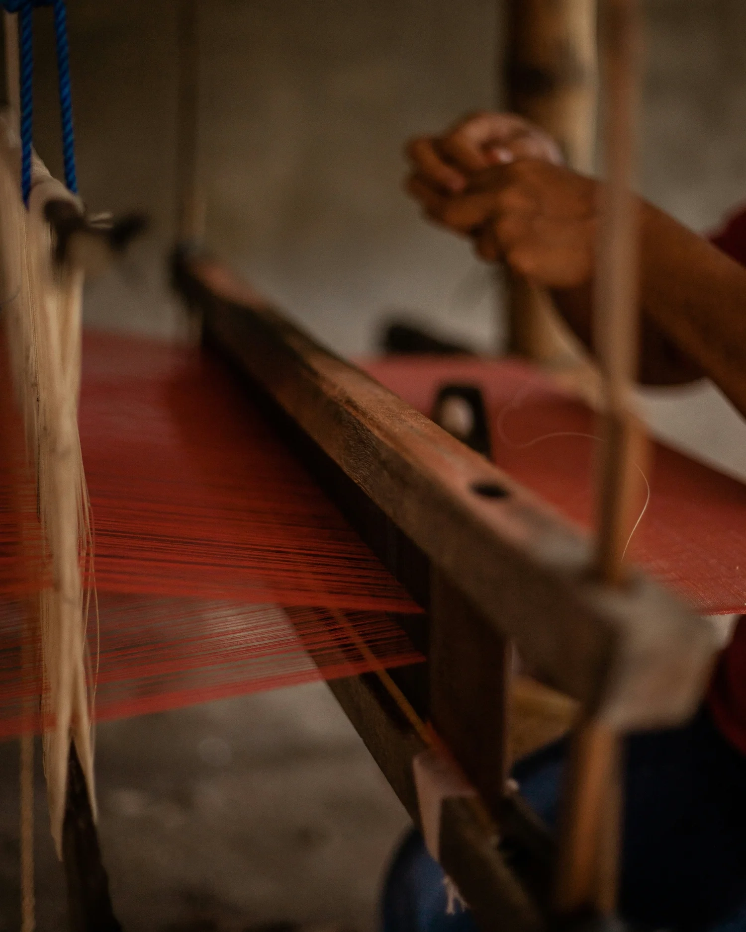 Hands working on a traditional loom with red threads