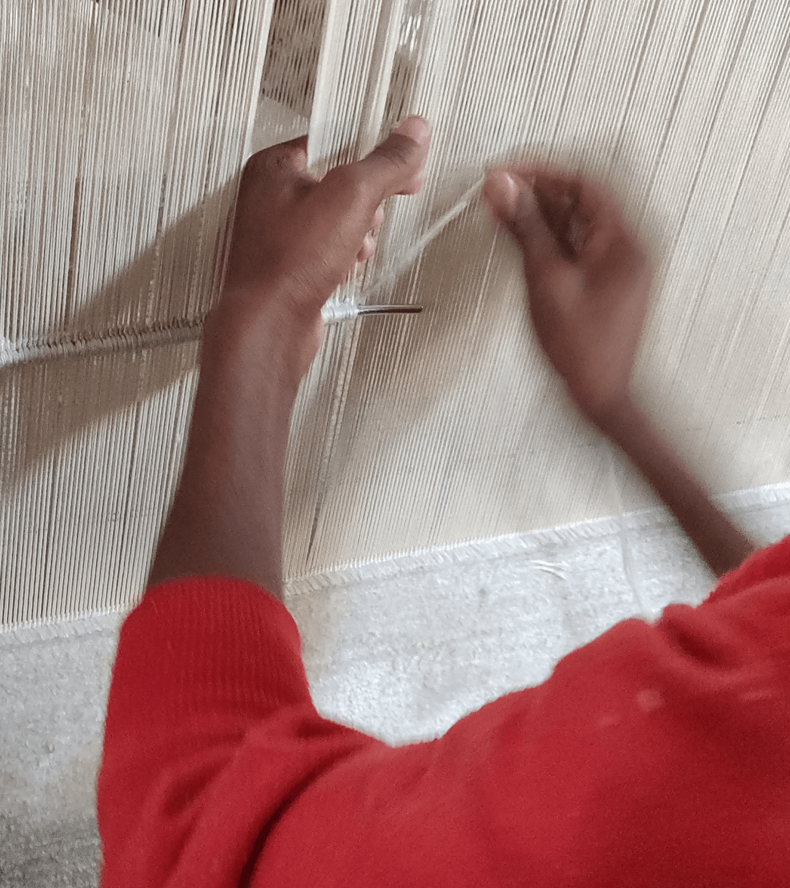 Close-up of hands weaving a rug with red garment